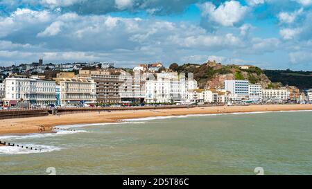 Hastings Castle und Seafront, England. Die Strandpromenade zur East Sussex Stadt Hastings mit seinem Wahrzeichen Burg sichtbar auf dem Hügel. Stockfoto