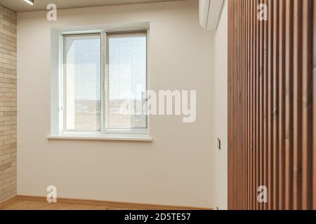 Das helle Zimmer mit einem Fenster, mit dunkelbraunen Holzlatten und einer Ziegelwand mit Klimaanlage und Steckdosen dekoriert Stockfoto