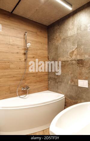 Badezimmer in einem Stil Loft mit Holz und Steinfliesen In warmen Tönen mit der weißen Eckbadewanne und einem Wasser aus silbernem Wasserhahn Stockfoto