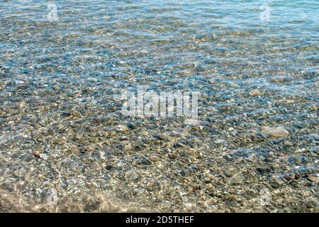 Klares Wasser und Steine. Farbige Kieselsteine unter klarem Meerwasser. Transparentes Wasser in flachen Gewässern auf See. Sauberes Wasser im Meer. Naturkonzept mit Stockfoto