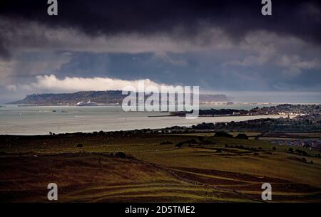 Eine dramatische Landschaft der Isle of Portland & Weymouth in Dorset England, aufgenommen von den umliegenden Hügeln, während die Sonne an einem stürmischen Tag durchbricht. Stockfoto