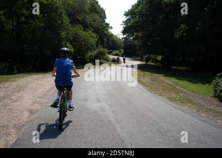 Ein Teenager folgt seiner Familie, hinkt aber hinterher Eine Landstraße im New Forest Hampshire England an Eine Fahrradtour mit der Familie Stockfoto