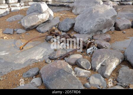 Eine ganze Hinterachse von einem zerstörten Auto an der Küste inmitten der Felsen an diesem schönen Ort in Südwales. Stockfoto