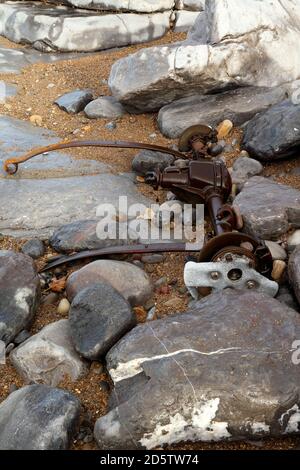 Eine ganze Hinterachse von einem zerstörten Auto an der Küste inmitten der Felsen an diesem schönen Ort in Südwales. Stockfoto