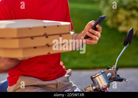 Smartphone- und Pizzaboxen in Kurierhänden, zugeschnittenes Bild. Selektiver Fokus. Konzept für die Lebensmittelzustellung Stockfoto