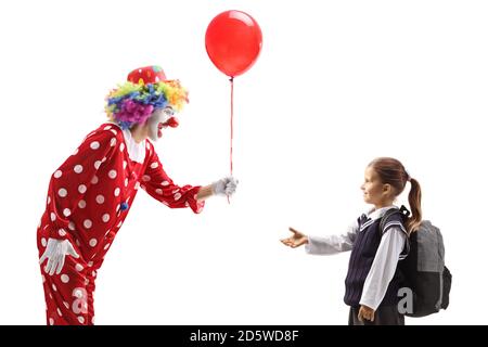 Fröhlicher Clown, der einem isolierten Schulmädchen einen roten Ballon gibt Auf weißem Hintergrund Stockfoto