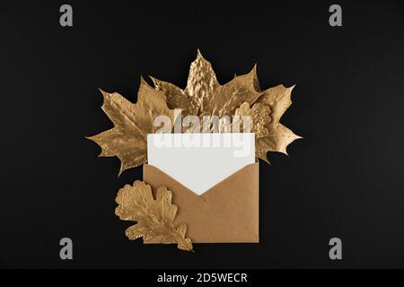 Umschlag mit Brief und glänzenden goldenen Ahornblättern auf schwarzem Hintergrund. Flach liegend, Draufsicht. Minimaler Herbst Komposition Konzept. Stockfoto
