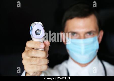 Coronavirus Symptome, Mann in medizinische Maske misst Körpertemperatur. Arzt mit einem digitalen isometrischen berührungslosen Thermometer in der Hand Stockfoto