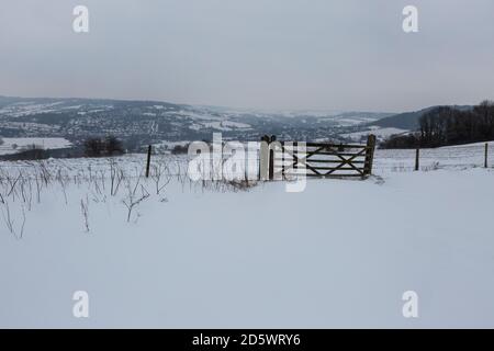 Tor mit Zaun in einer schneebedeckten hügeligen Landschaft Stockfoto