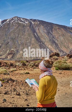 Mädchen liest eine Wanderkarte vor dem el Teide. Vulkan el Teide auf Teneriffa, Spanien. Mädchen mit Wanderkarte vor el Teide. Stockfoto