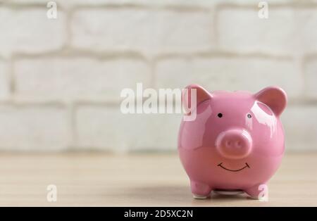 Pink Piggy Bank auf einem Tisch oder Regal gegen eine helle Ziegelwand. Stockfoto
