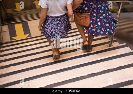 Mutter und Tochter gehen die U-Bahn-Treppe hinunter, Pfeile auf dem Boden in der neuen Normalität, soziale Distanz zu halten. Stockfoto