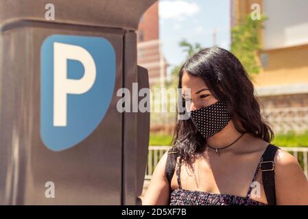 Junge Frau trägt Schutzmaske mit Parkmaschine auf der Straße. Stockfoto