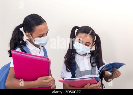 Schülerinnen tragen medizinische Maske Blick auf das Notebook. Schule während der Coronavirus-Infektion. Kleine Mädchen studieren. Stockfoto