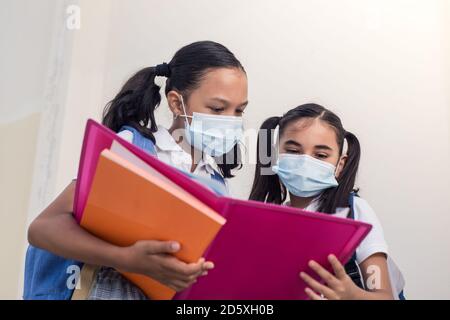 Schulkind mit Notizbüchern in den Händen Lesen und Studieren. Kleine Mädchen mit Gesichtsmaske vor Coronavirus zu schützen. Stockfoto