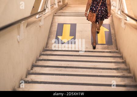 Junge Frau trägt ein Kleid geht die Treppe hinunter mit Bodenpfeilen auf neue normale mit sozialen Distanzierung. Stockfoto