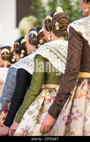 Vertikales Foto einer Gruppe von Falleras in einer Reihe von hinten gesehen. Kleider mit floralen Mustern und typischer Frisur der fallas mit ihren Schmuckstücken. Stockfoto