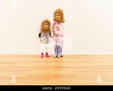 Zwei Mädchen mit Affen Masken stehen Hand in Hand Vorderseite der weißen Wand Stockfoto