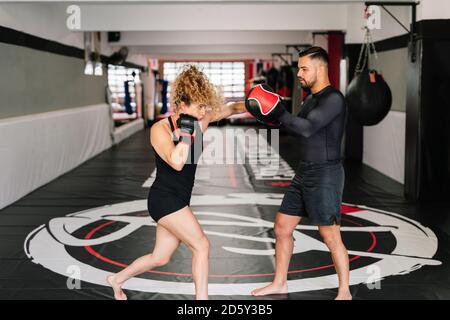 Boxerin trainiert mit ihrem hochkonzentrierten Trainer in Rot Boxhandschuhe schlagen direkt in die Hände des Trainers in einem Fitnessraum Stockfoto