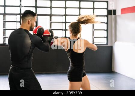 Boxerin trainiert mit ihrem hochkonzentrierten Trainer in Rot Boxhandschuhe stanzen und beugen sich direkt an den Händen des Trainers In einem Fitnessstudio Stockfoto