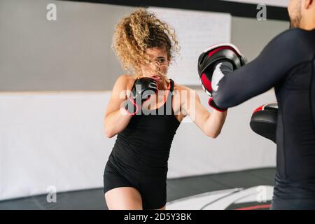 Boxerin trainiert mit ihrem hochkonzentrierten Trainer in Rot Boxhandschuhe schlagen direkt in die Hände des Trainers in einem Fitnessraum Stockfoto