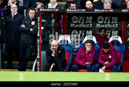 Manchester City Manager Pep Guardiola (unten links) Im Dugout neben Assistenztrainer Domenec Torrent und Trainer Mikel Arteta (rechts) Stockfoto