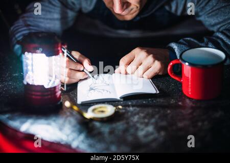 Mann, der in Estland campt und nachts sein Skizzenbuch zeichnet Stockfoto