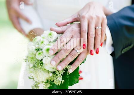 Braut und Bräutigam zeigen Eheringe, halten Bouquet Stockfoto