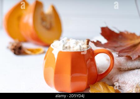 Komposition mit orangefarbenem Kürbis-Stil Tasse Kaffee mit Marshmallows und Herbstdeko, gefallenen Blättern, gemütlichem Pullover auf weißem Hintergrund. Stockfoto