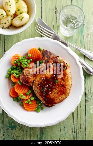 Schweinekotelett mit Karotten, Erbsen und Kartoffeln auf Teller Stockfoto