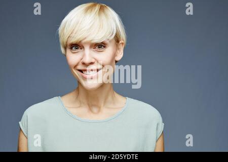 Porträt von lächelnden blonden Frau vor grauem Hintergrund Stockfoto