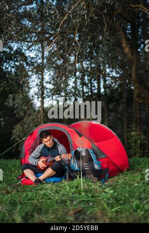 Mann, der in Estland zeltet, in seinem Zelt sitzt und die Ukulele spielt Stockfoto