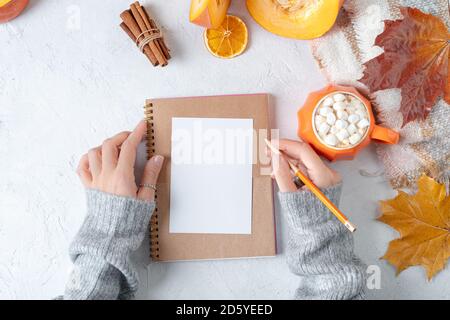 Desktop-Modell-Planer. Draufsicht Komposition mit Frauenhänden in Pullover, Kürbisse, Tasse Kaffee mit Marshmallows und Herbstdekoration, gefallen l Stockfoto