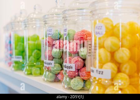 Beschriftete Glasgläser mit grünen, gelben, roten und blauen Süßigkeiten auf einem weißen Regal in einem Süßwarenladen. Stockfoto