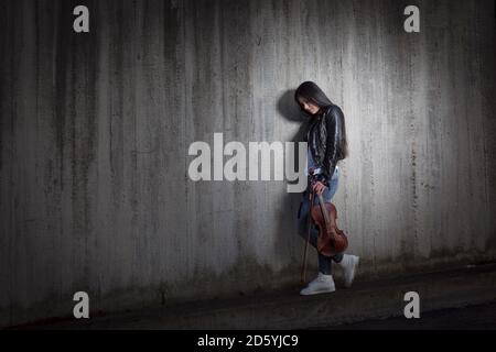 Junge asiatische Geigerin an Betonwand gelehnt Stockfoto