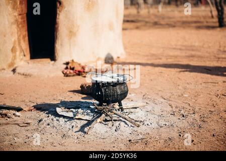 Namibia, Damaraland, Eisentopf Kochen auf kleinem Feuer vor eine Hütte in einem Himba-Dorf Stockfoto