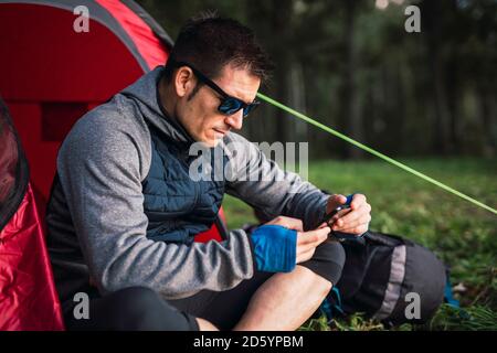 Mann, der in Estland zeltet, im Zelt sitzt, mit dem Smartphone Stockfoto