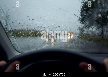 Fahren bei starkem Regen. Regentropfen auf der Windschutzscheibe des Autos gegen den Verkehr an der Kreuzung. Stockfoto