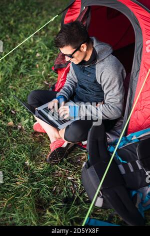 Mann, der in Estland zeltet, im Zelt sitzt, mit Laptop Stockfoto