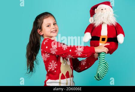 frohe weihnachten. Weihnachtsstimmung Konzept. Weihnachtstraditionen. Lieber Weihnachtsmann. Kleines Kind tragen Santa Spielzeug blauen Hintergrund. Kleines Mädchen Spielzeug vorhanden. Winterurlaub. Geschenk bringt Freude und Glück. Stockfoto