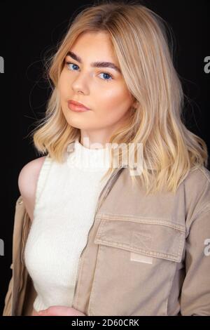 Eine schöne junge blonde Frau in ihren frühen Zwanzigern trägt eine braune Jacke und schaut direkt auf die Kamera. Stockfoto