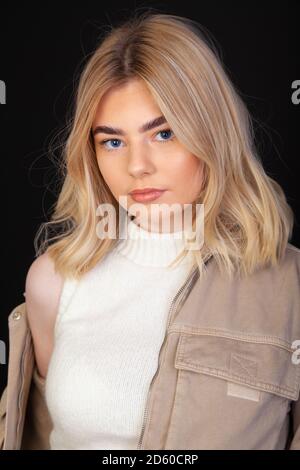 Eine schöne junge blonde Frau in ihren frühen Zwanzigern trägt eine braune Jacke und schaut direkt auf die Kamera. Stockfoto