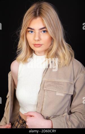 Eine schöne junge blonde Frau in ihren frühen Zwanzigern trägt eine braune Jacke und schaut direkt auf die Kamera. Stockfoto