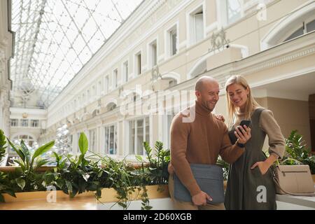 Junges Paar mit Handy, während er auf sein Mittagessen wartet Im Restaurant Stockfoto