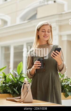 Junge Frau liest eine Nachricht auf dem Handy, während Kaffee trinken im Einkaufszentrum stehen Stockfoto