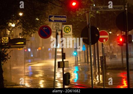 Regnerische Nacht in der Großstadt, Autos fahren auf der Straße. Unschärfes Bild. Ampeln und viele Straßenschilder im Vordergrund. Stockfoto