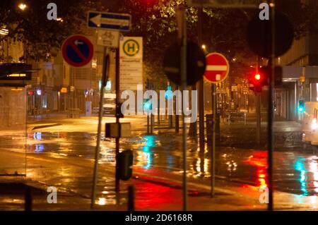 Regnerische Nacht in der Großstadt, Autos fahren auf der Straße. Unschärfes Bild. Ampeln und viele Straßenschilder im Vordergrund. Stockfoto