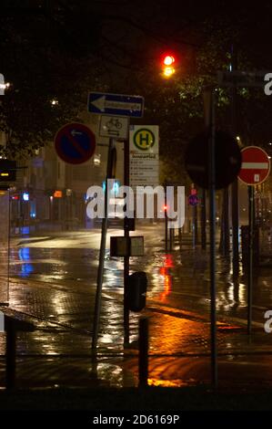 Regnerische Nacht in der Großstadt, Autos fahren auf der Straße. Unschärfes Bild. Ampeln und viele Straßenschilder im Vordergrund. Stockfoto