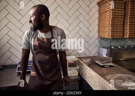 Fröhlicher junger männlicher Bäcker, der in der Pizzeria arbeitet Stockfoto
