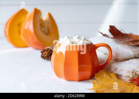 Komposition mit orangefarbenem Kürbis-Stil Tasse Kaffee mit Marshmallows und Herbstdeko, gefallenen Blättern, gemütlichem Pullover auf weißem Hintergrund. Stockfoto